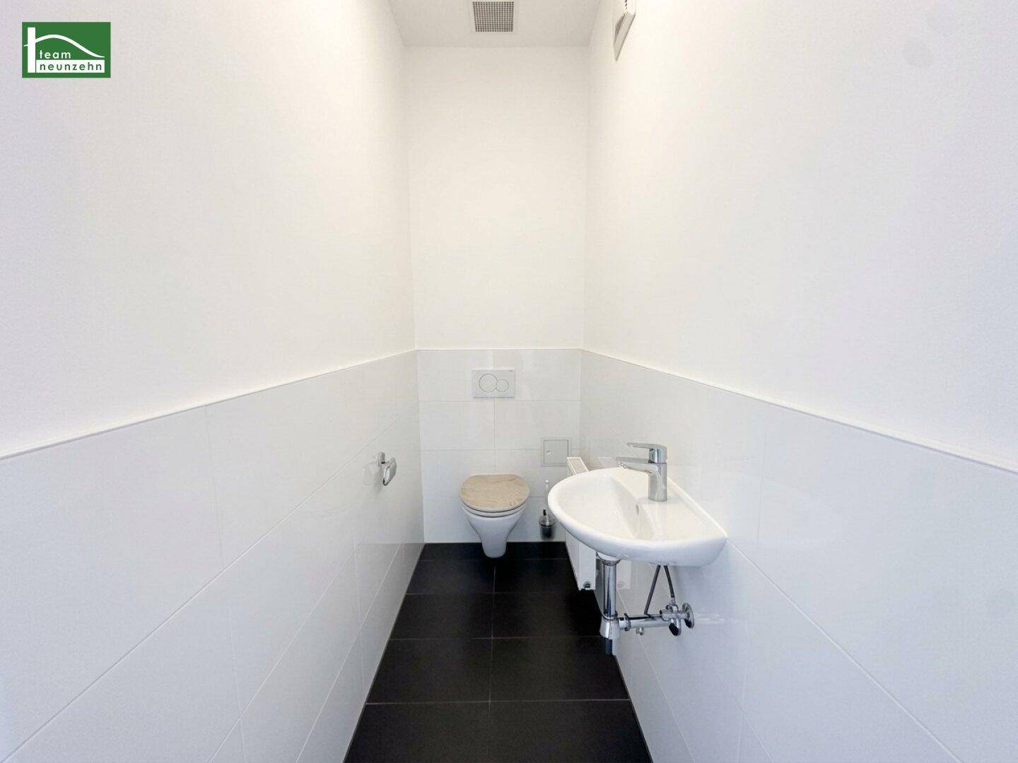 Kleines Gäste-WC mit Toilette, Waschbecken, weißen Fliesen und dunklem Fliesenboden.