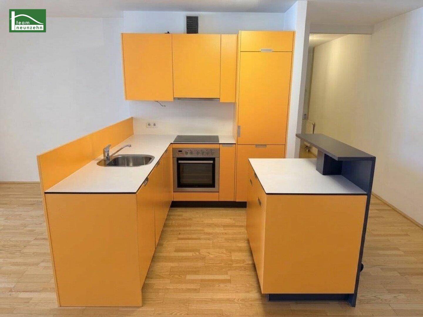 Funktionale Küche mit orangefarbenen Schränken, integrierten Geräten und einem kleinen Tresen.