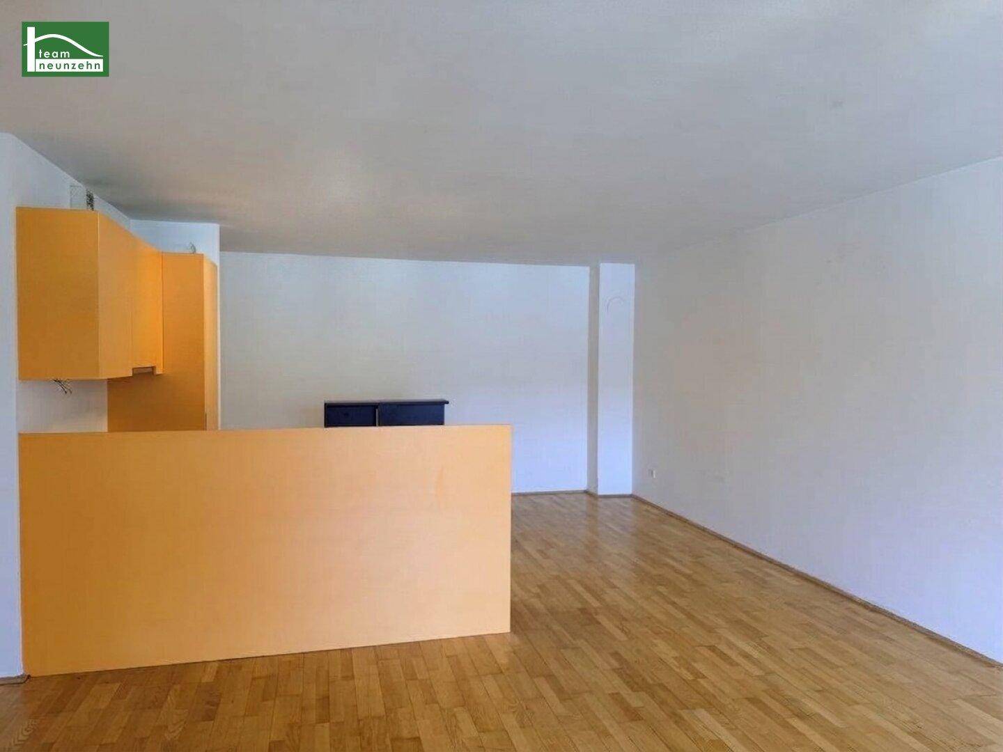Offener Wohnbereich mit Parkettboden und einer halb offenen Küche mit Tresen.