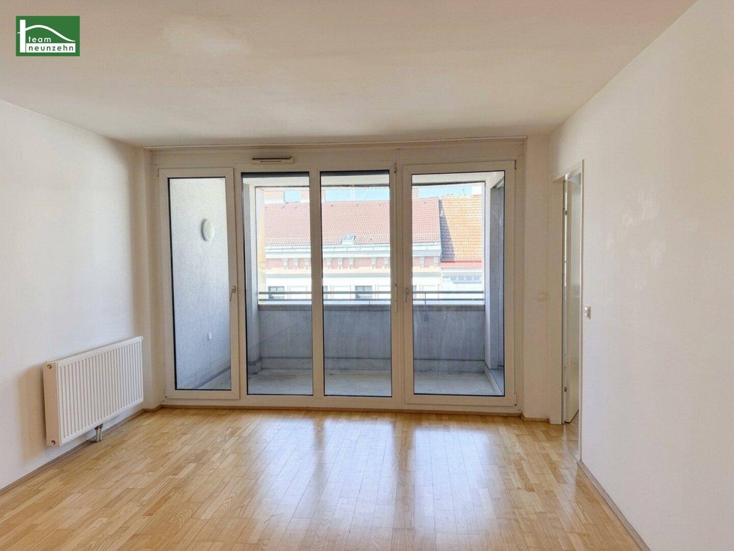 Helles Zimmer mit Parkettboden, weißen Wänden und großen Fenstern zum Balkon.
