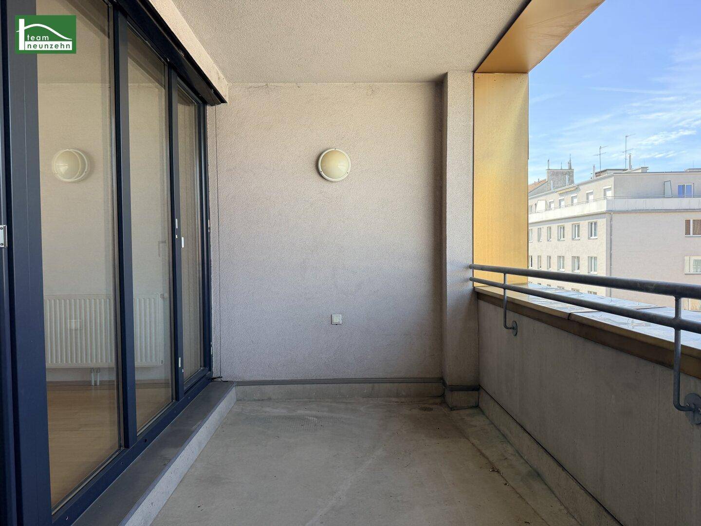 Geräumiger Balkon mit Betonboden und Metallgeländer, bietet einen Blick auf die Umgebung.