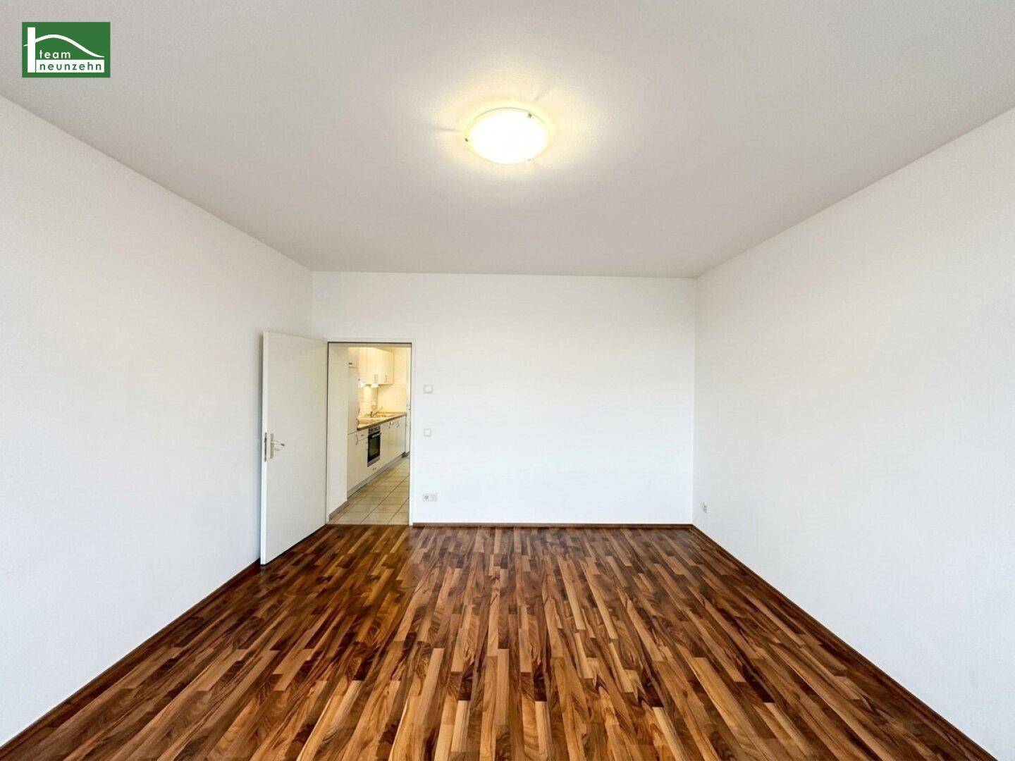 Geräumiges Zimmer mit Holzboden und Zugang zu einer angrenzenden Küche.