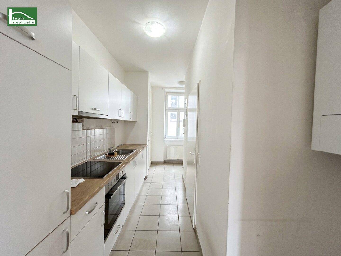 Funktionale Küche mit weißen Schränken, integriertem Backofen und Blick auf ein Fenster.
