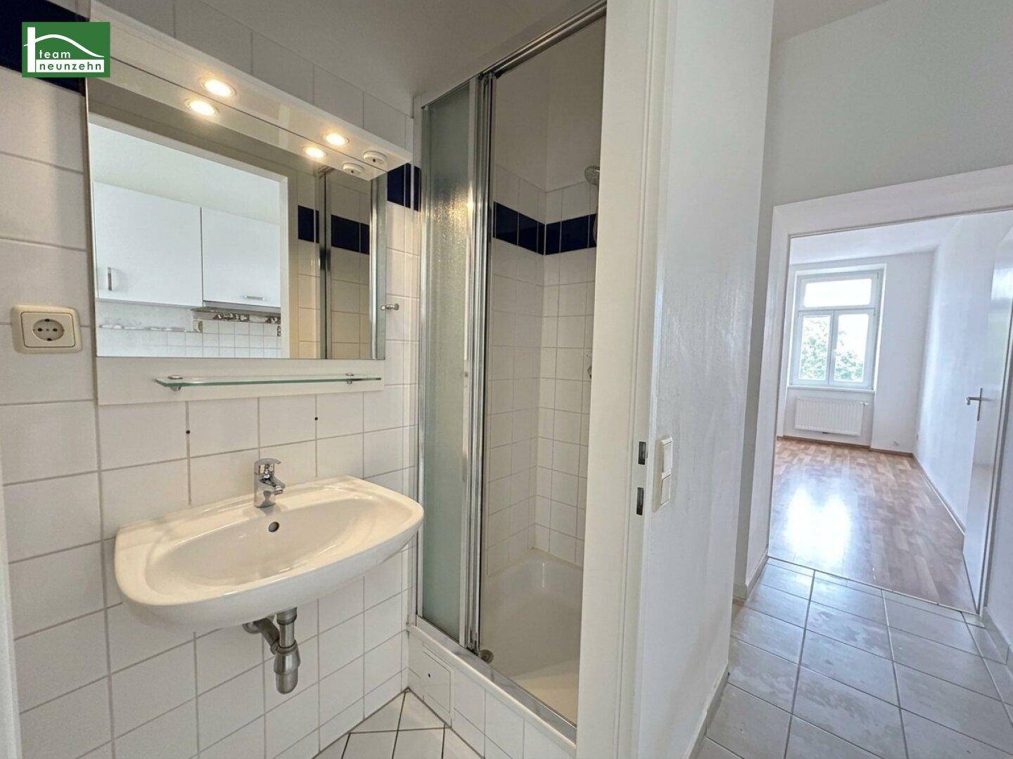 Badezimmer mit Dusche, Waschbecken und Spiegel, hell gefliest und funktional.