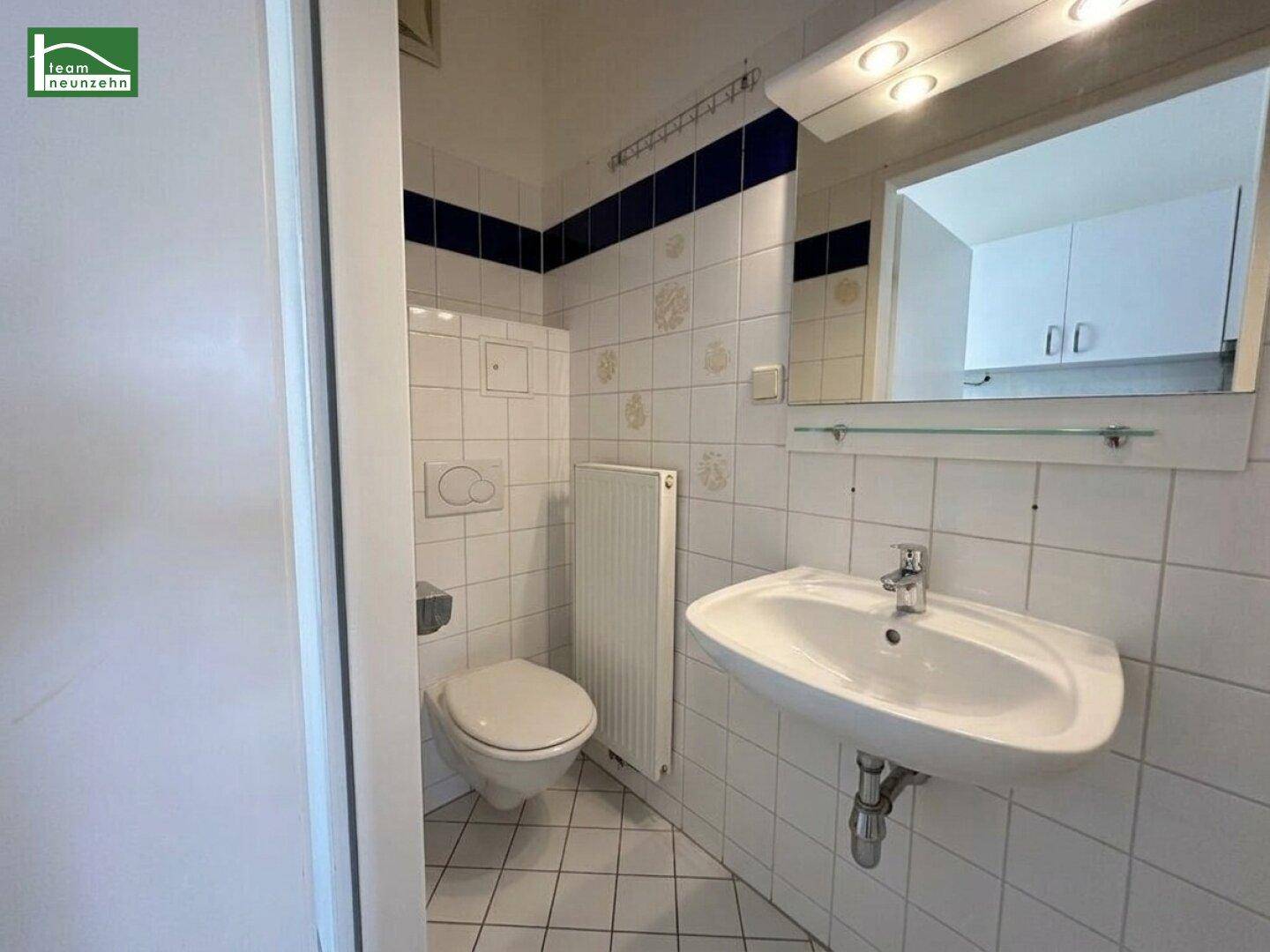 Kleines Badezimmer mit WC, Waschbecken und Spiegel, komplett gefliest.