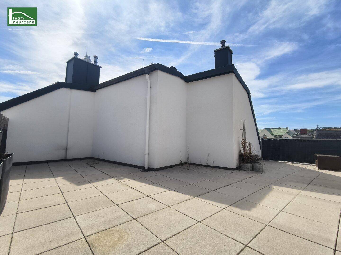 Geräumige Dachterrasse mit hellen Fliesen und Blick auf die Umgebung unter blauem Himmel.