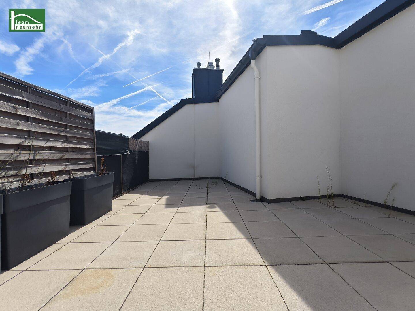 Weitläufige Dachterrasse mit hellen Fliesen und einem Sichtschutz aus Holz.