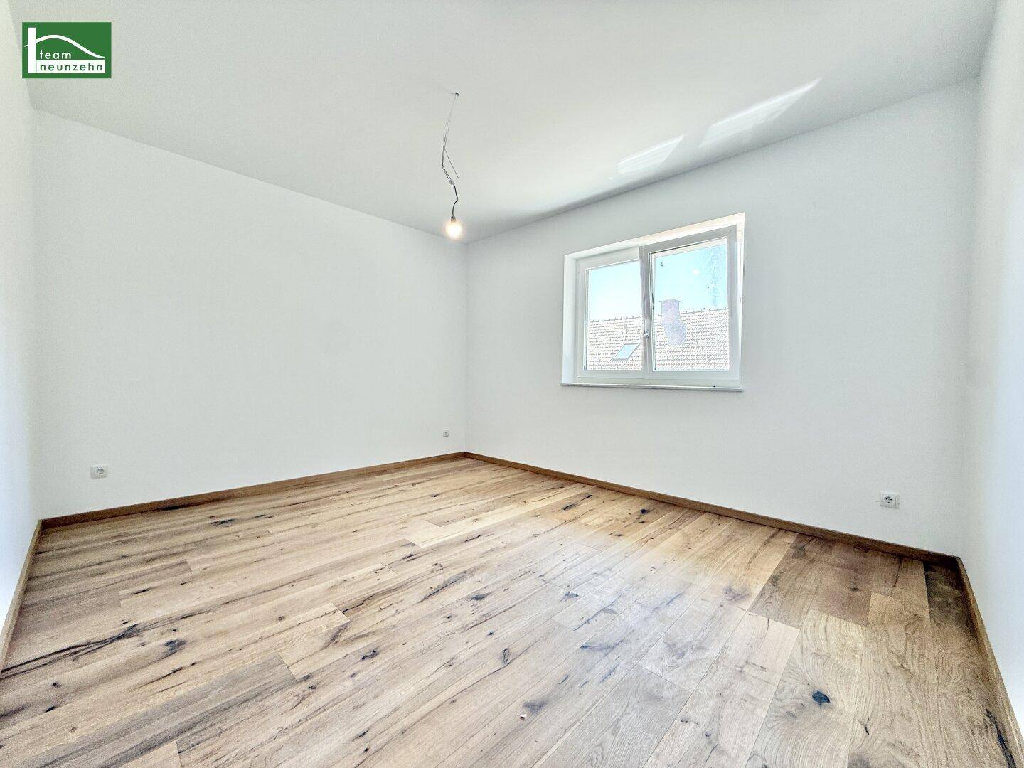 Geräumiges Schlafzimmer mit Holzboden und Blick ins Grüne durch das Fenster.