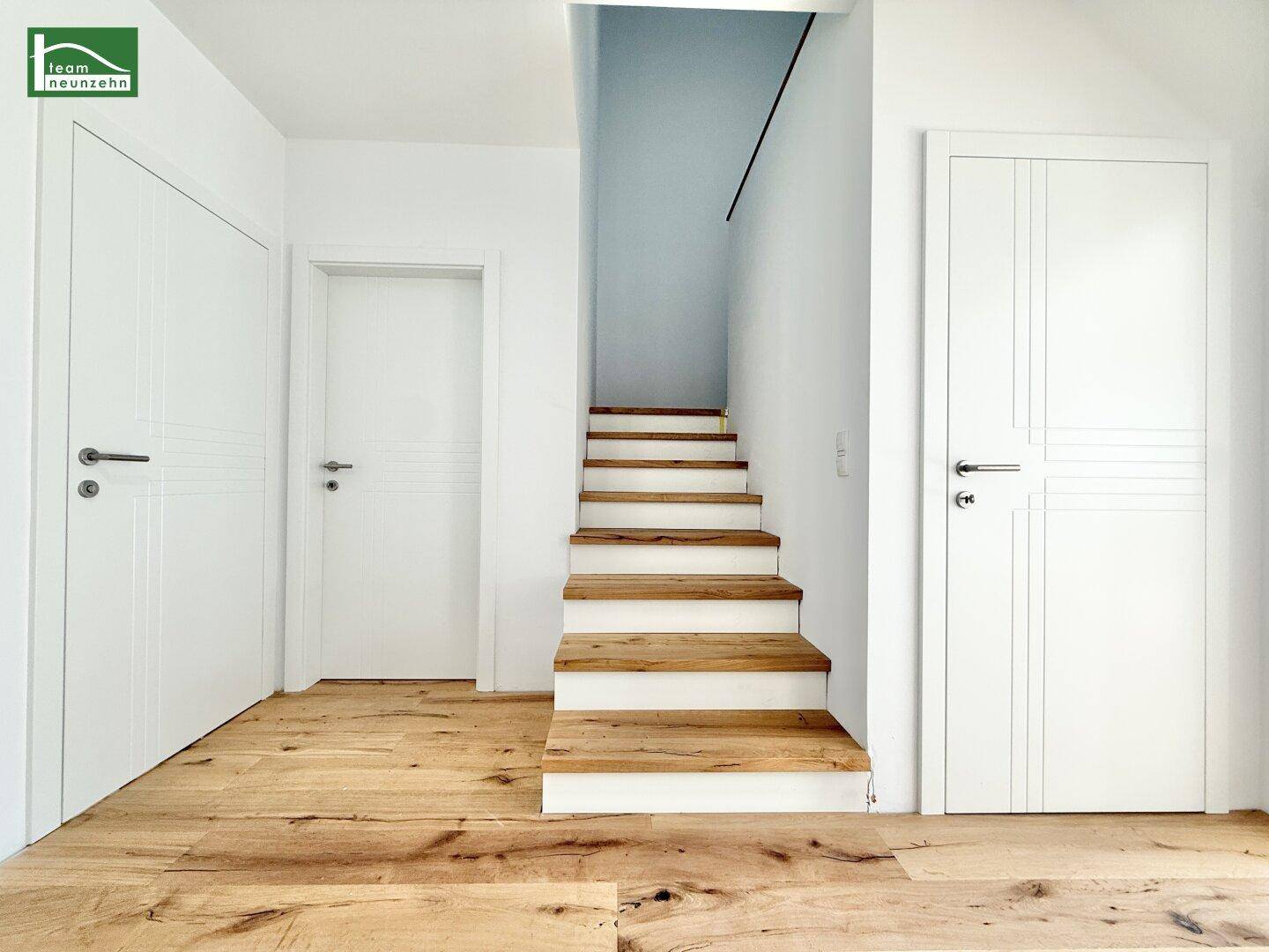Moderner Eingangsbereich mit Holztreppe und weißen Türen.
