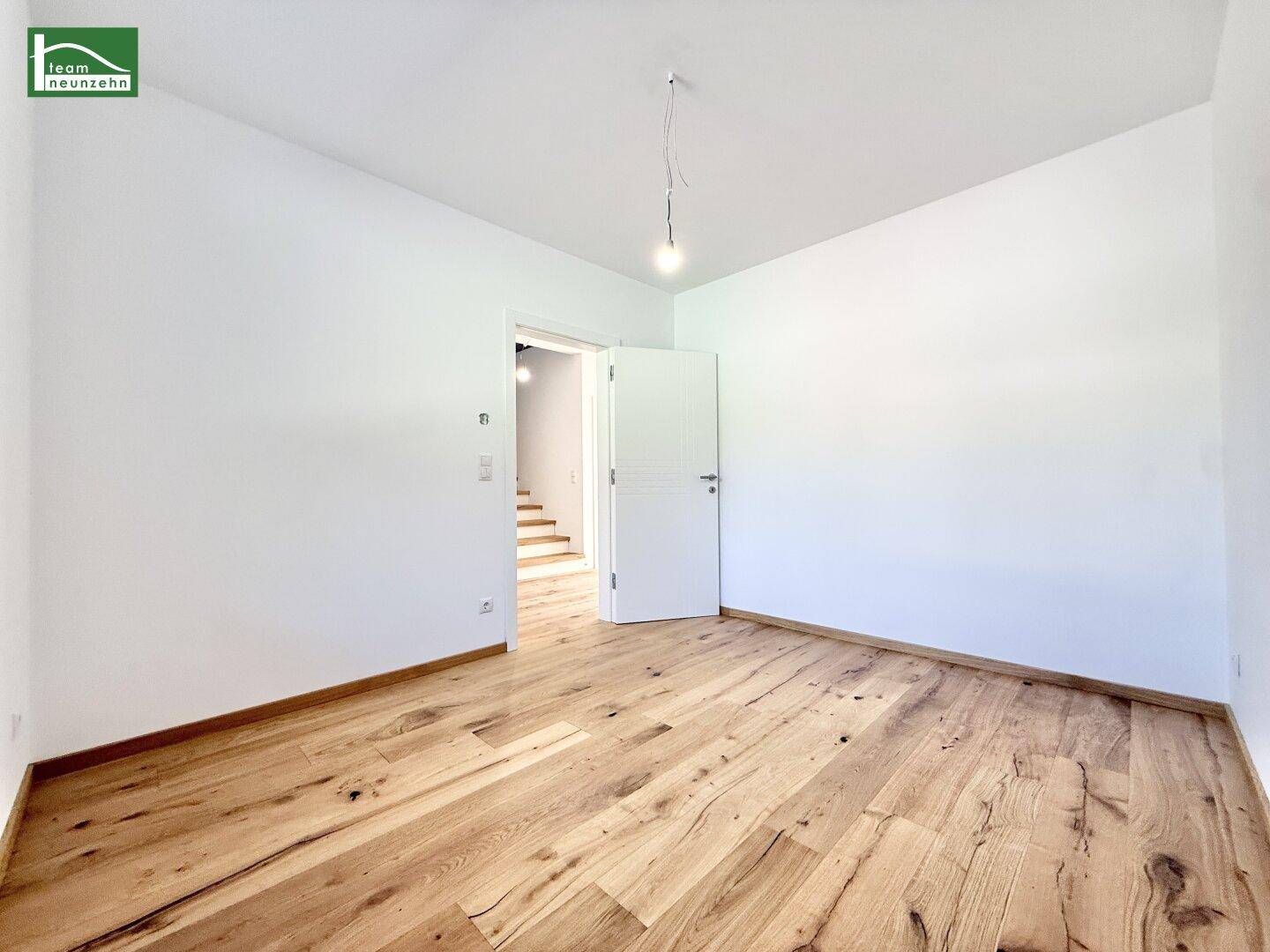 Helles Schlafzimmer mit Holzboden und Zugang zum Treppenhaus.