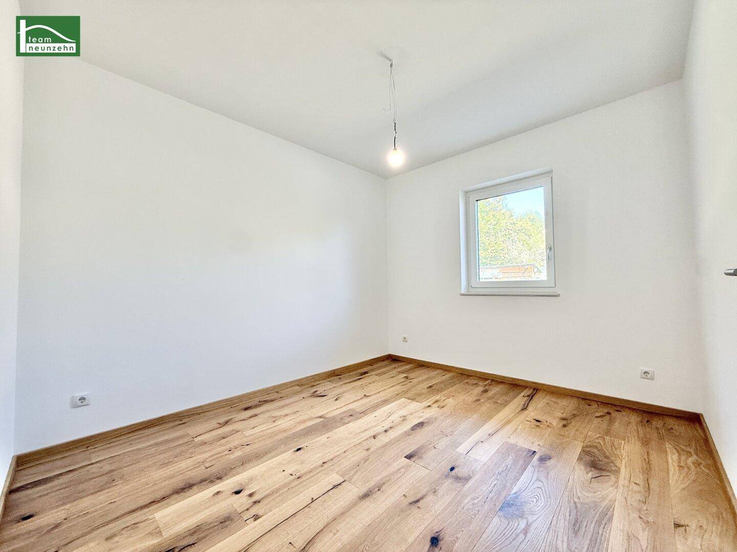 Geräumiges Schlafzimmer mit Fenster und durchgehendem Holzboden.