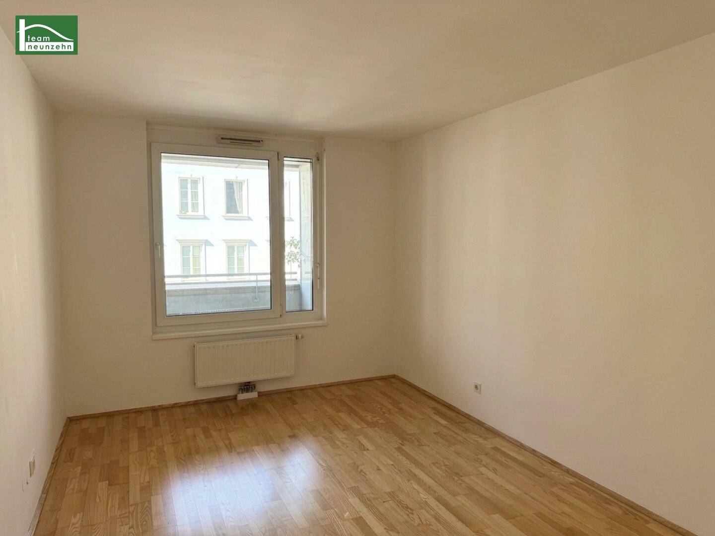 Gemütliches Schlafzimmer mit Parkettboden und einem großen Fenster, das viel Licht hereinlässt.