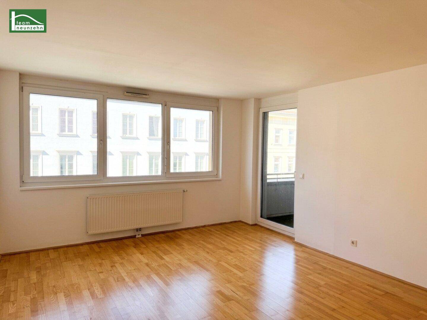 Helles Zimmer mit Parkettboden, großen Fenstern und direktem Zugang zu einem Balkon.