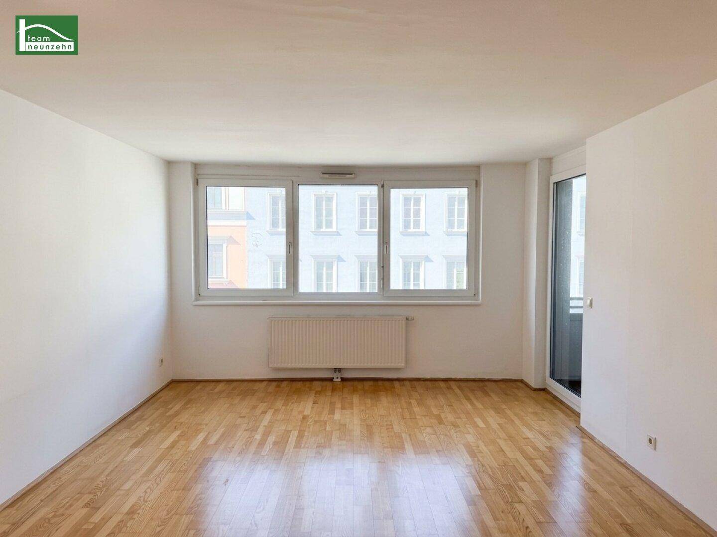 Geräumiges Zimmer mit viel Tageslicht durch die breite Fensterfront und Holzboden.