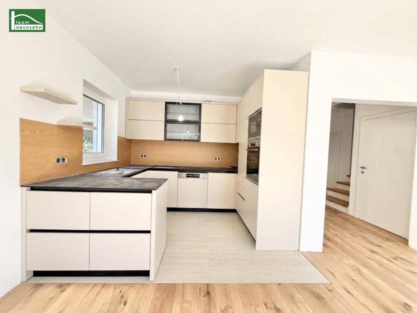 Moderne Einbauküche mit hellen Fronten, dunkler Arbeitsplatte und Holzakzenten im Neubau.