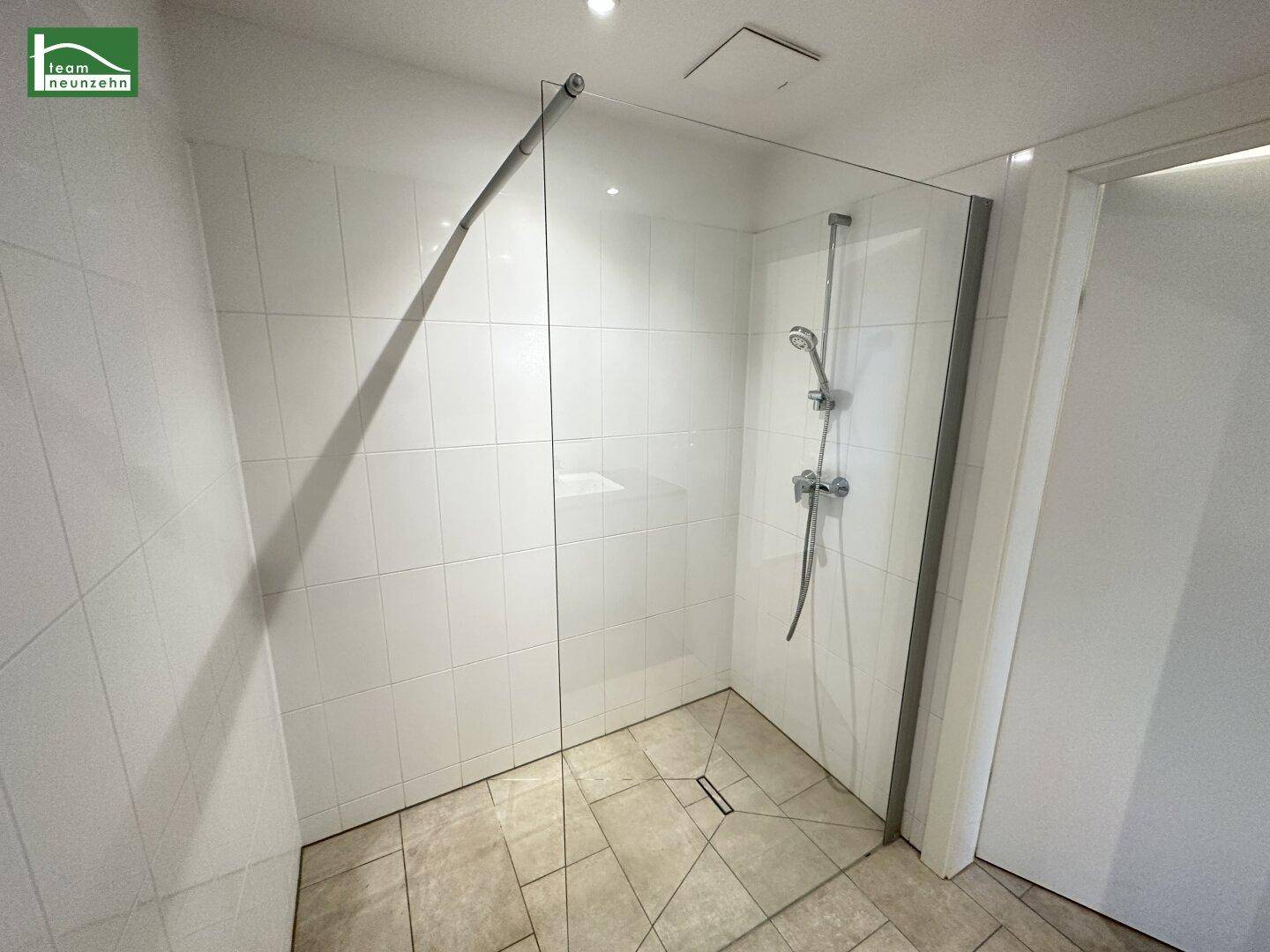 Modernes Badezimmer mit begehbarer Dusche, Glasabtrennung und weißen Fliesen.