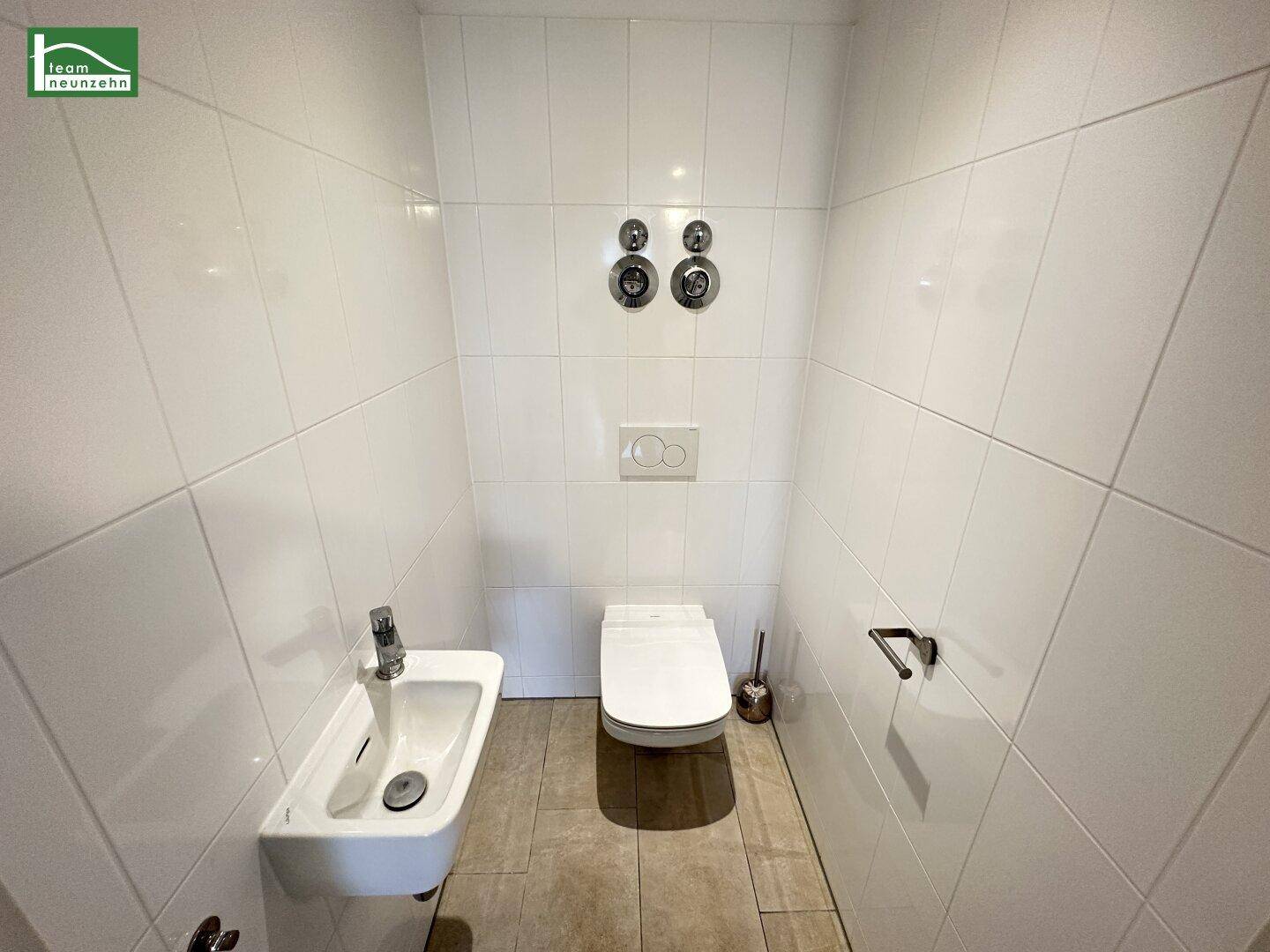 Separates WC mit wandhängender Toilette und kleinem Handwaschbecken.