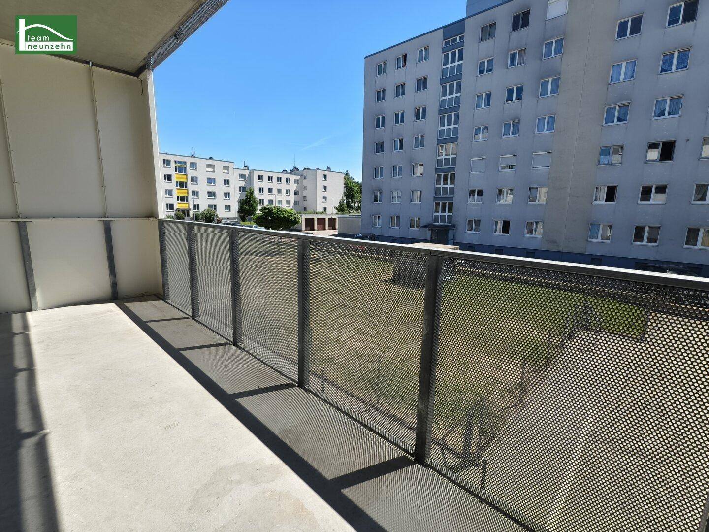 Balkon mit Metallgeländer und Blick auf die umliegenden Wohngebäude und Grünflächen.