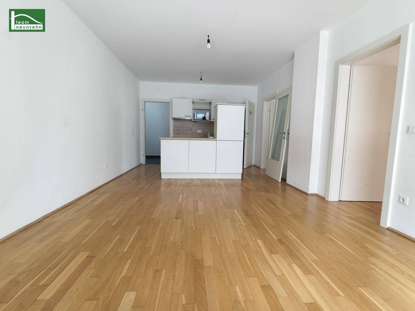 Offener Wohnbereich mit Parkettboden und integrierter Küchenzeile im Hintergrund.
