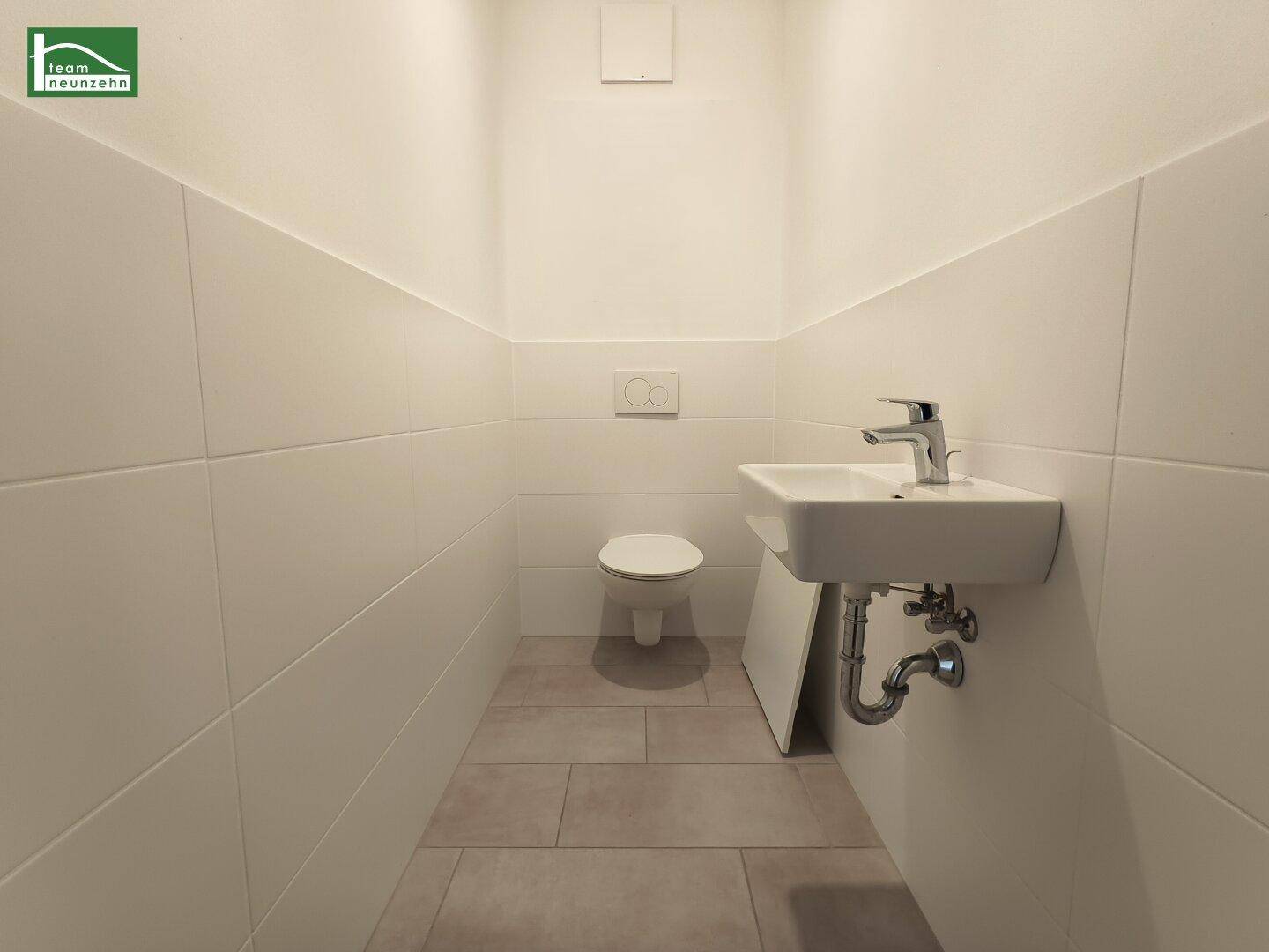 Separates Gäste-WC mit wandhängender Toilette und kleinem Handwaschbecken.