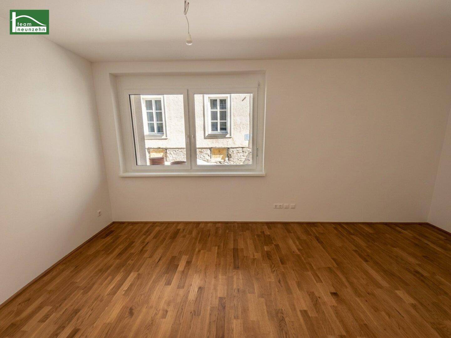 Heller, unmöblierter Raum mit Parkettboden und Blick auf die umliegenden Gebäude.