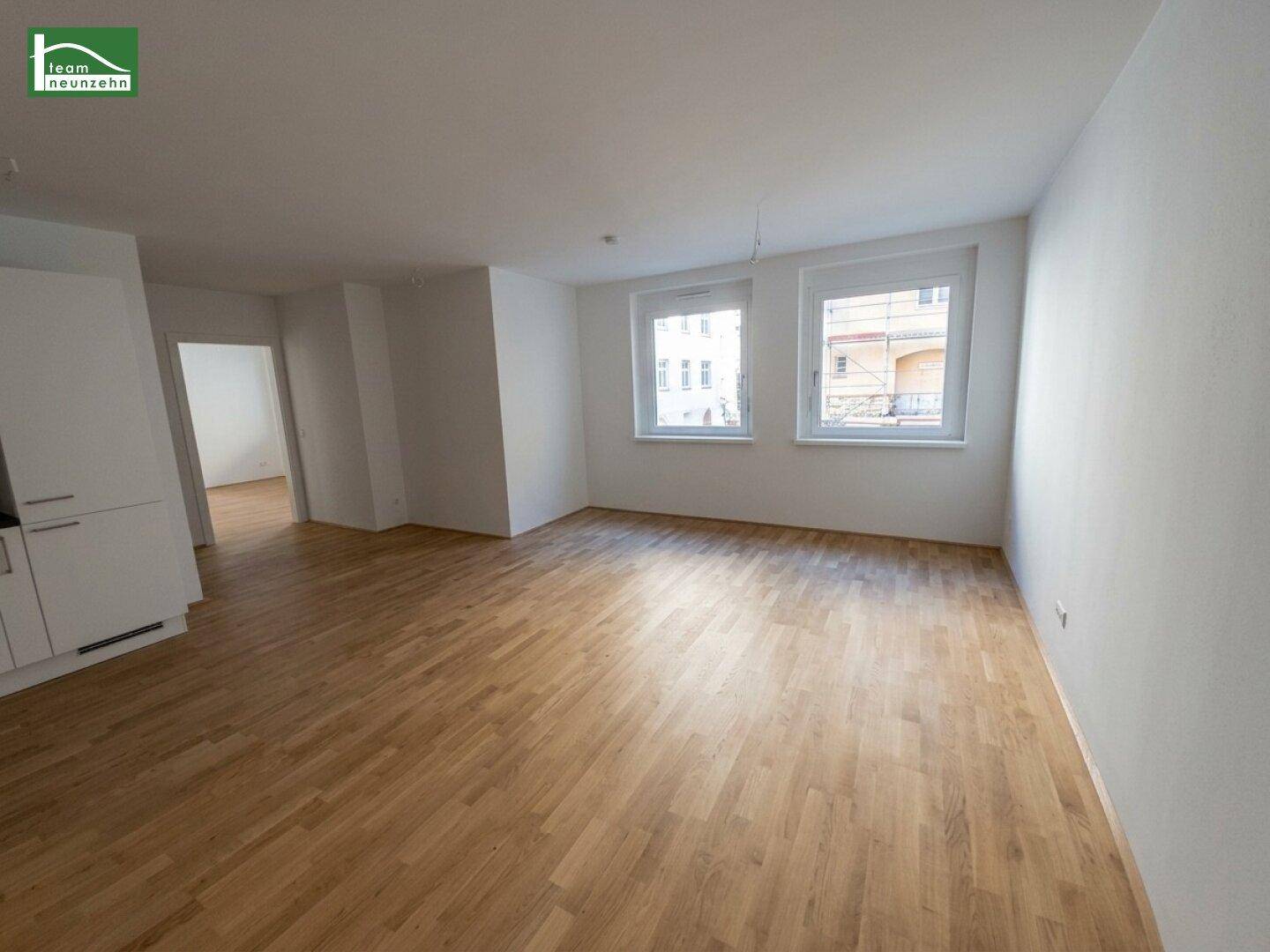 Geräumiger, leerer Wohn-Essbereich mit hellem Parkettboden und großen Fenstern.