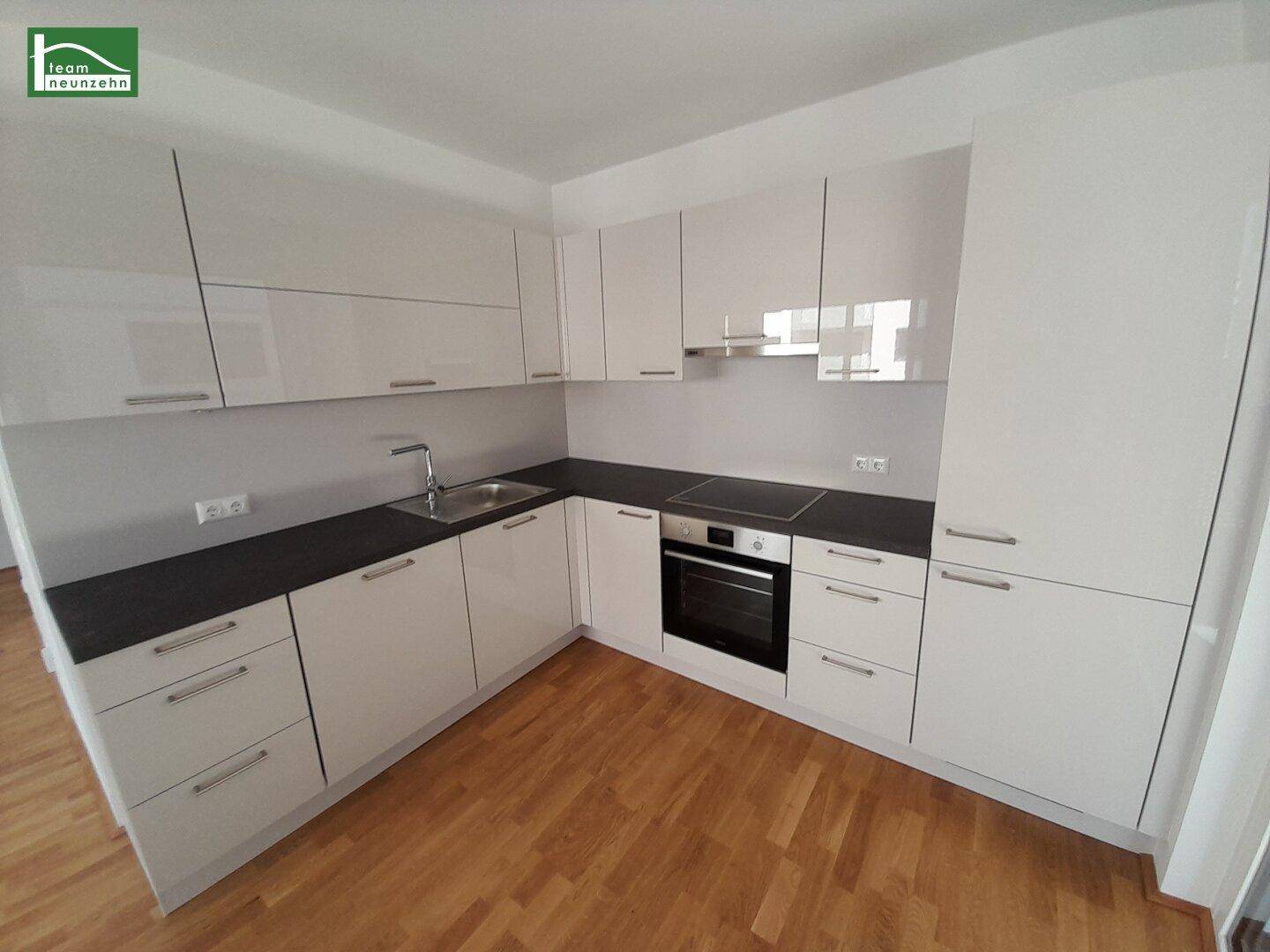 Moderne Einbauküche mit weißen Hochglanzfronten, dunkler Arbeitsplatte und integrierten Geräten.