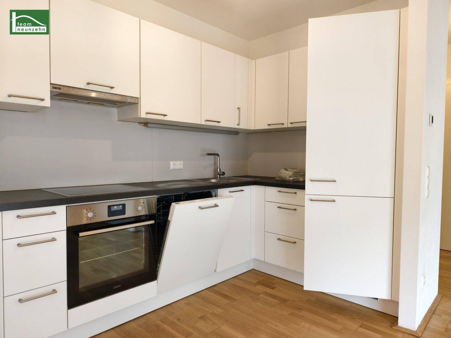 Moderne Einbauküche mit weißen Schränken, dunkler Arbeitsplatte und integrierten Geräten.