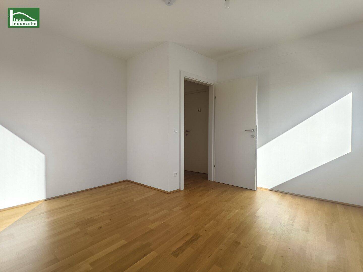 Leerer Raum mit Parkettboden und weiß gestrichenen Wänden, der Zugang zu einem weiteren Zimmer bietet.