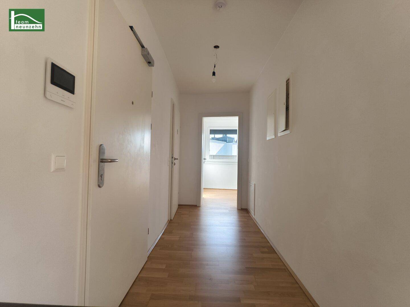 Heller Flur mit Holzboden, weiß gestrichenen Wänden und einer modernen Eingangstür.