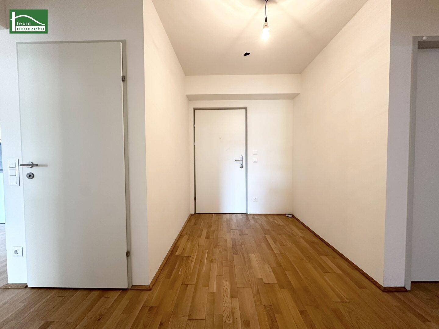 Heller Eingangsbereich mit Holzboden und weißen Türen, der zu den Zimmern führt.