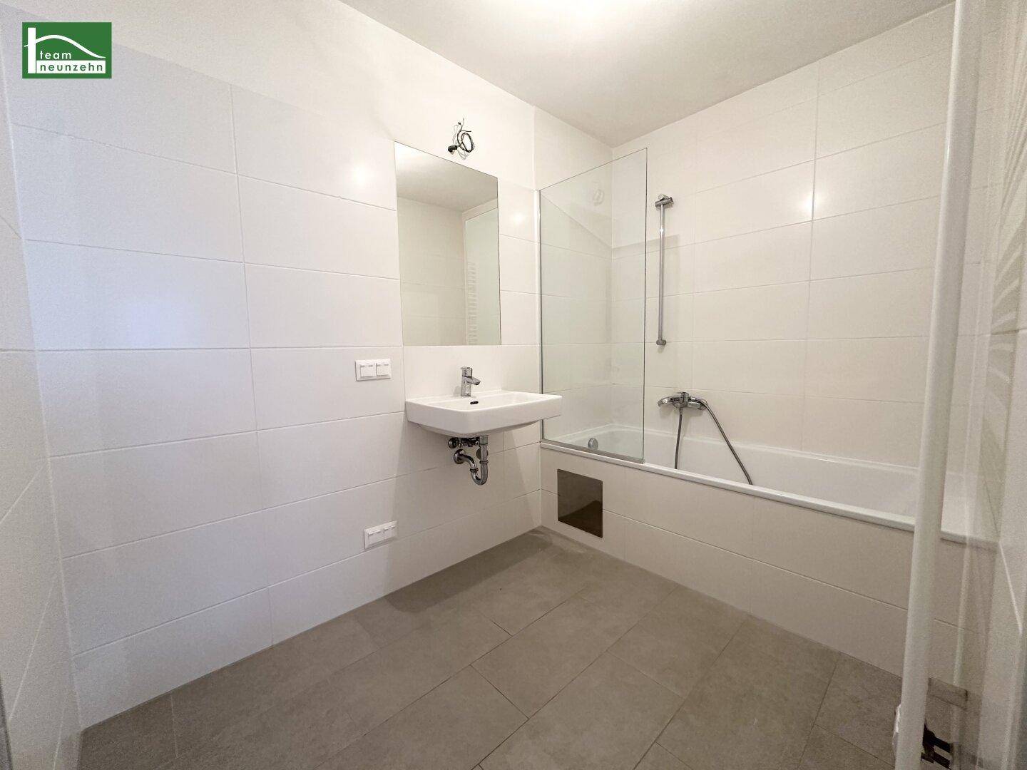 Modernes Badezimmer mit weißen Fliesen, Badewanne und Duschabtrennung aus Glas.