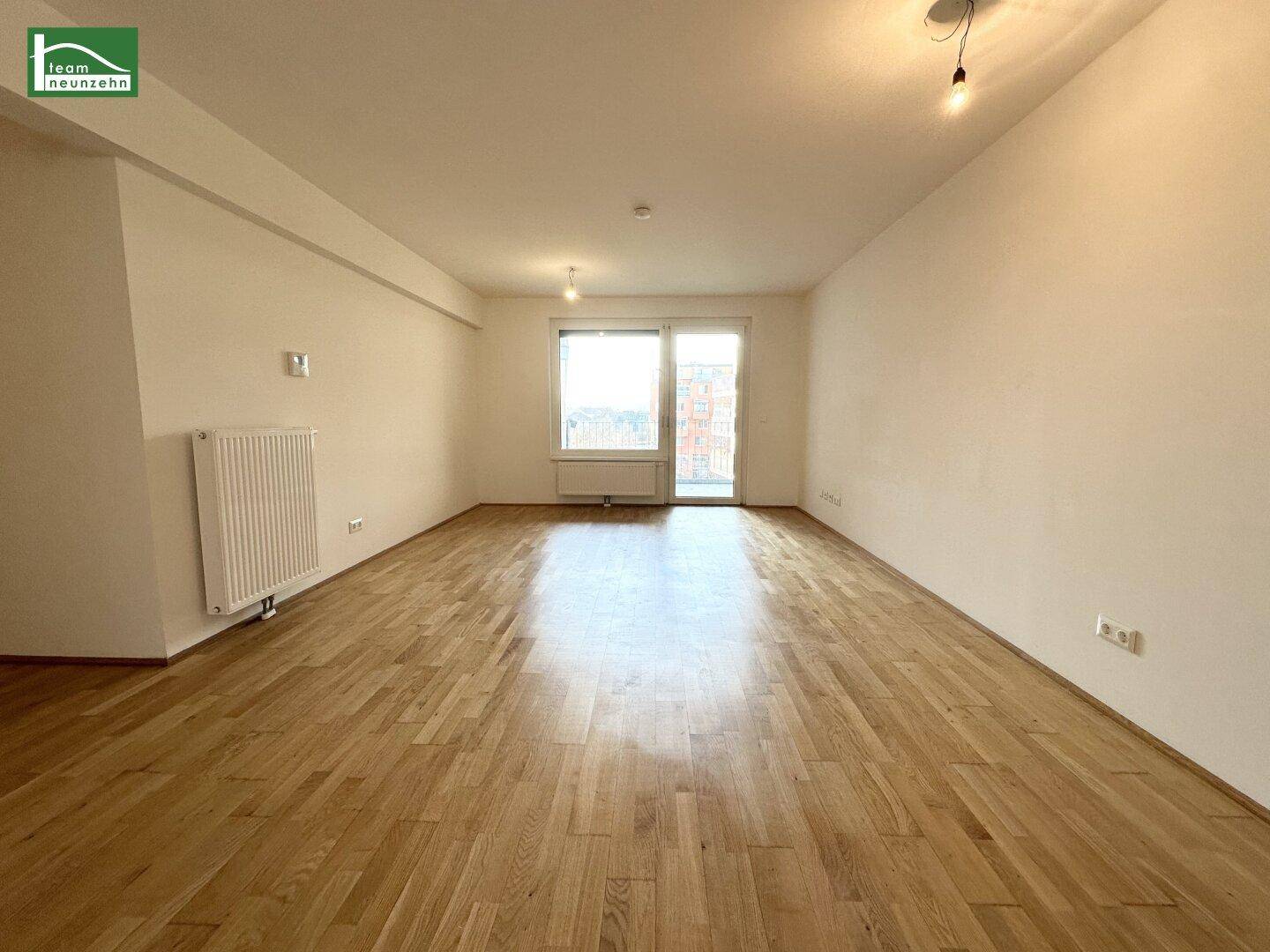 Geräumiger, leerer Wohn- und Essbereich mit hellem Holzboden und großen Fenstern.