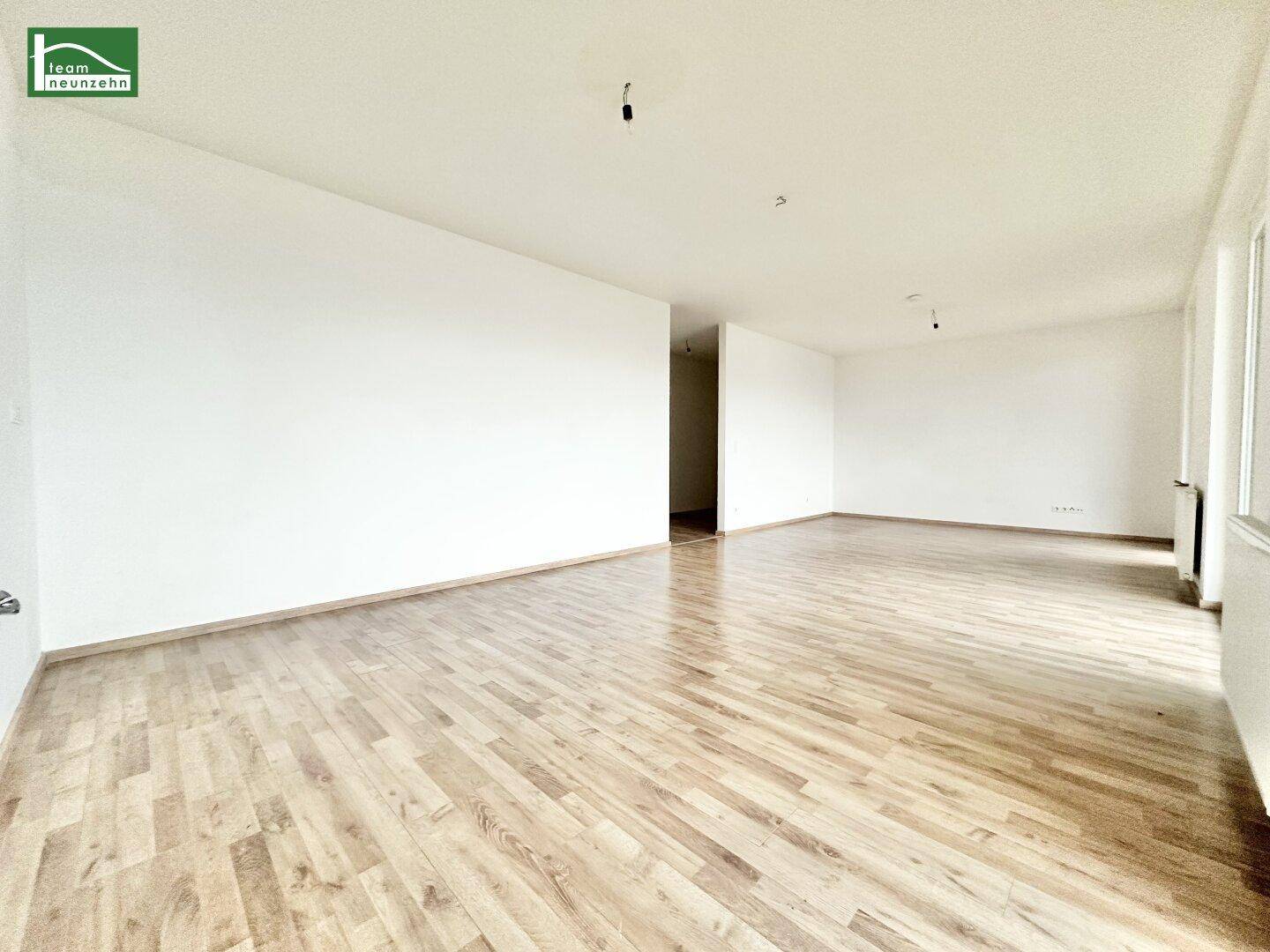 Geräumiges, unmöbliertes Wohnzimmer mit hellem Laminatboden und weißen Wänden.