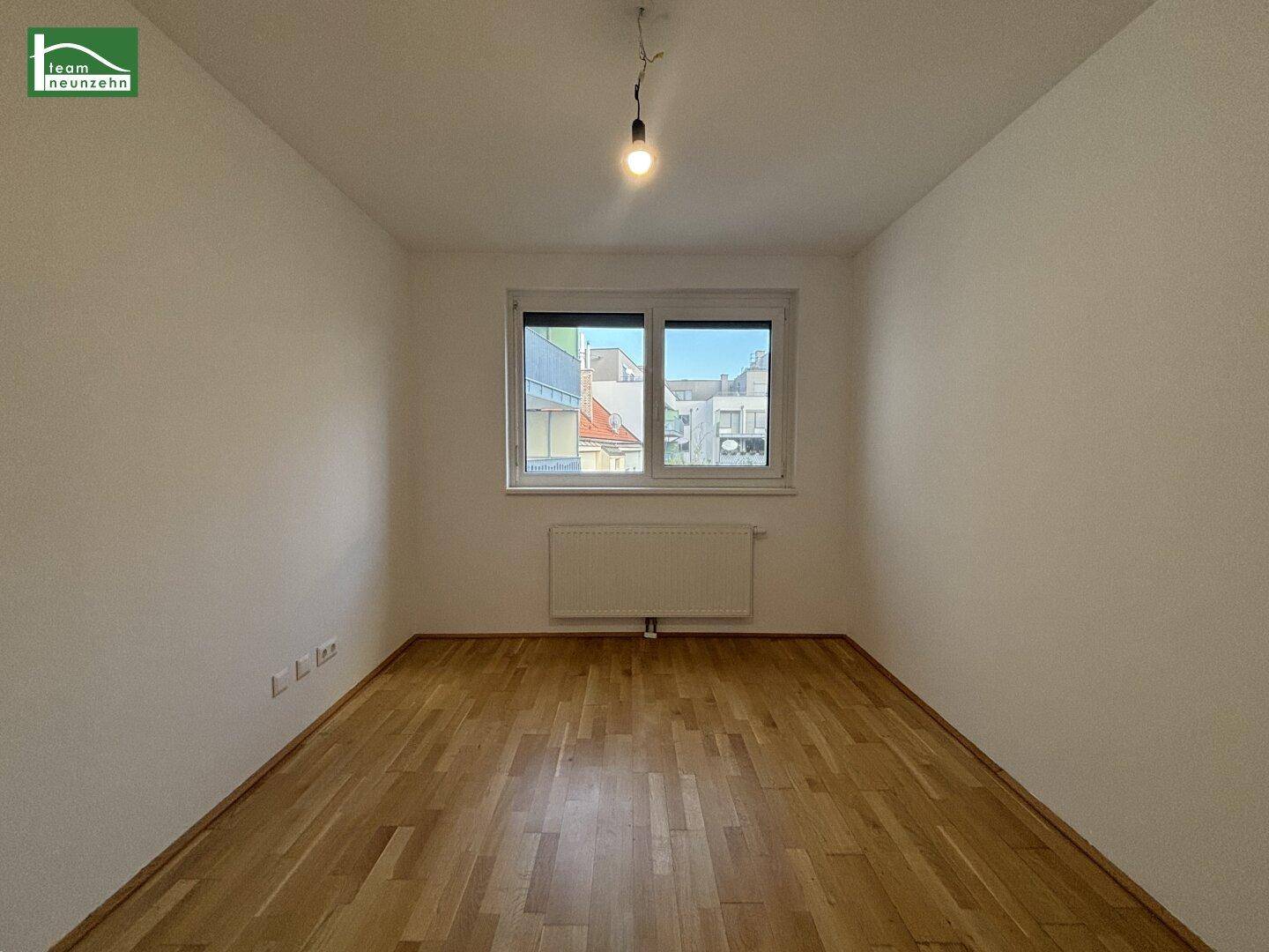 Leeres Zimmer mit Holzboden und Fenster, das einen Blick auf die Umgebung bietet.