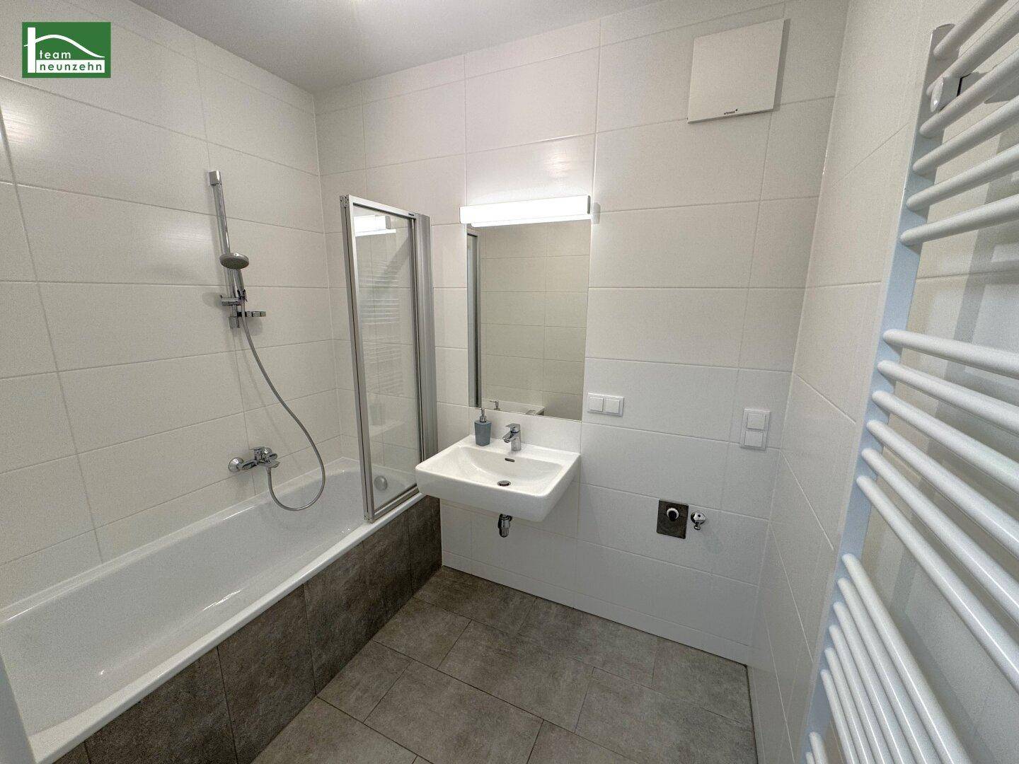 Leeres Badezimmer mit Badewanne, Duschabtrennung, Waschbecken und beheiztem Handtuchhalter.