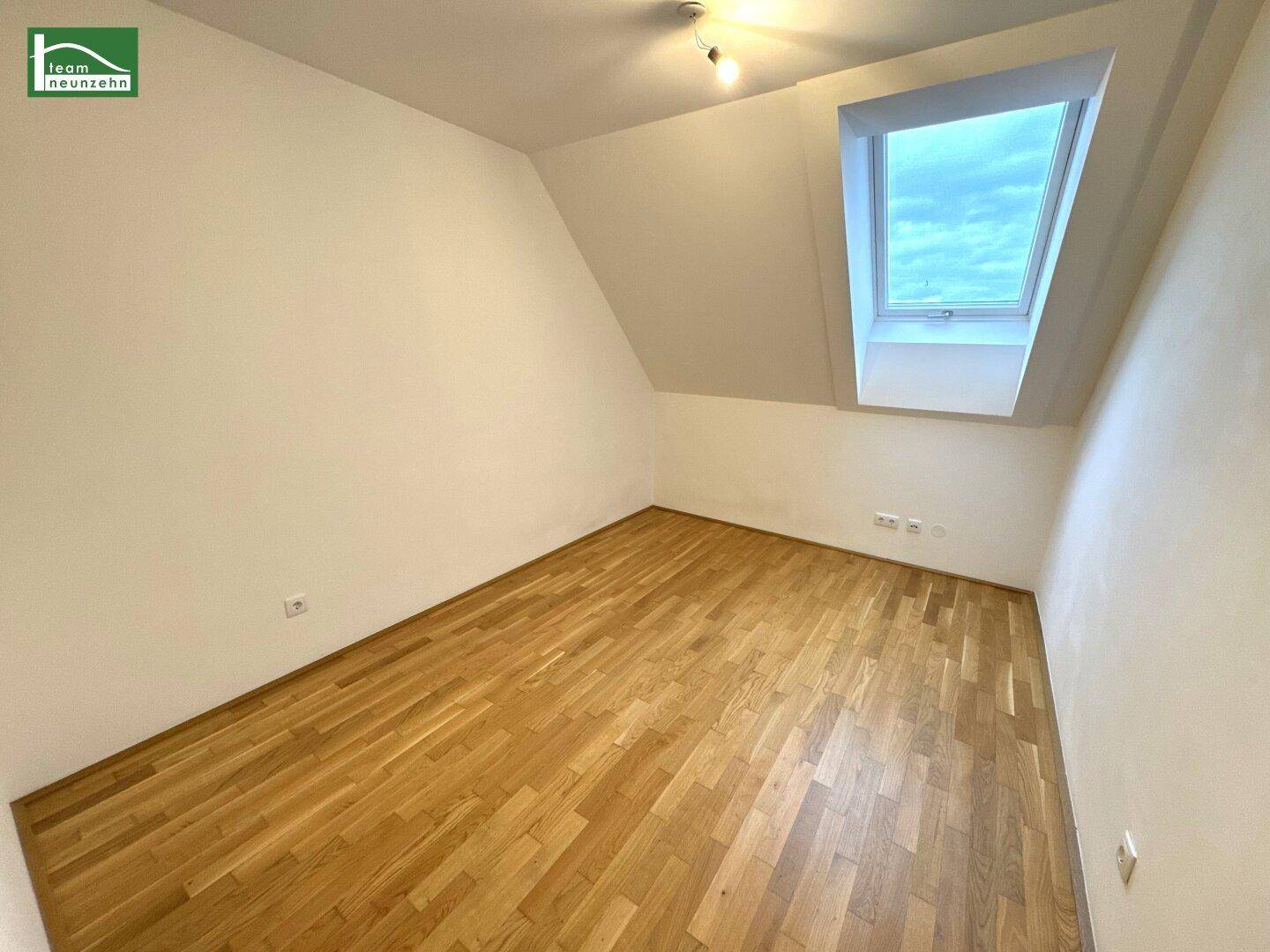 Leeres Schlafzimmer im Dachgeschoss mit Parkettboden und einem großen Dachfenster.