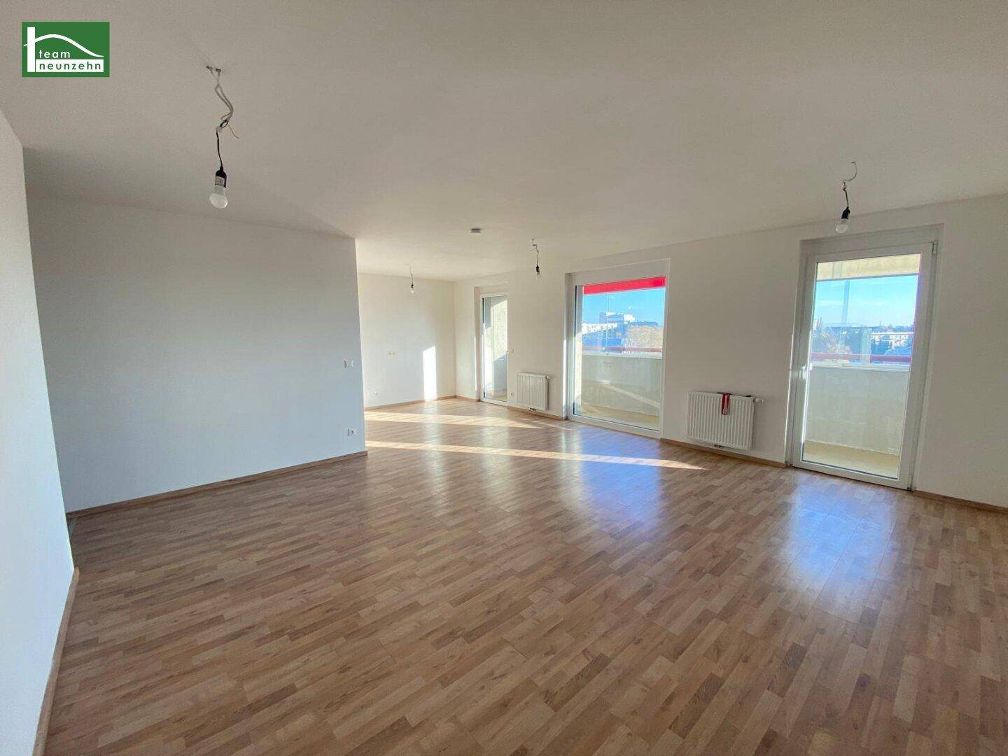 Heller, unmöblierter Wohnraum mit Parkettboden und Zugang zu einem Balkon, bietet viel Tageslicht.