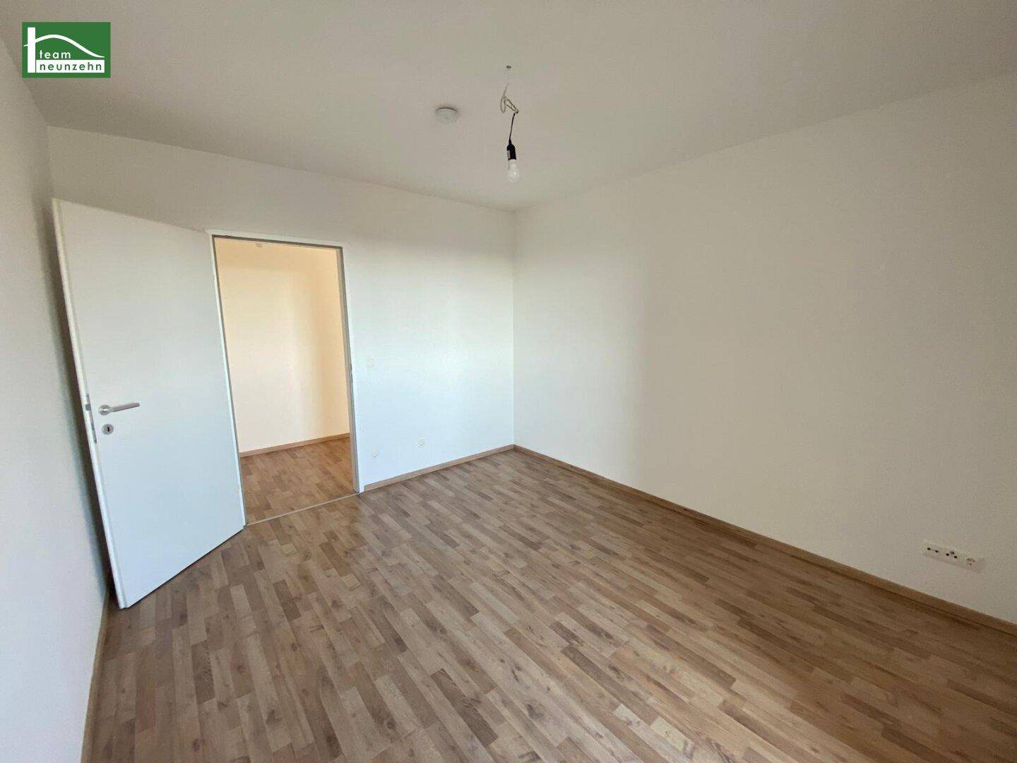Leeres Schlafzimmer mit Parkettboden und offener Tür zu einem weiteren Raum, bietet Flexibilität.