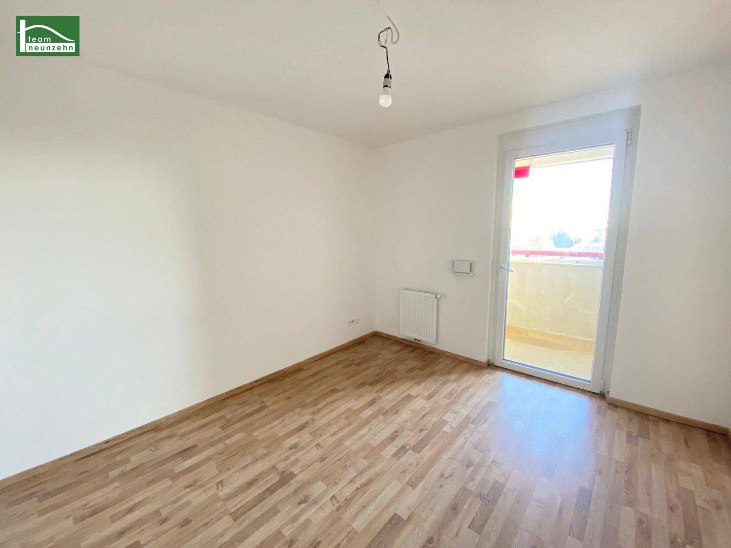 Helles, leeres Zimmer mit Laminatboden und direktem Zugang zu einem Balkon.