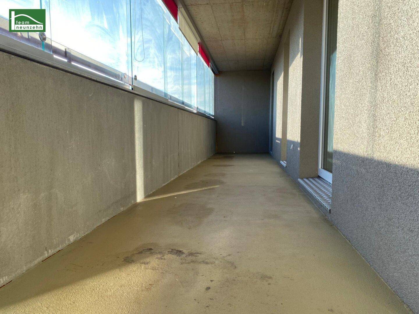 Lange, verglaste Loggia mit Betonboden, bietet geschützten Außenbereich und Ausblick.