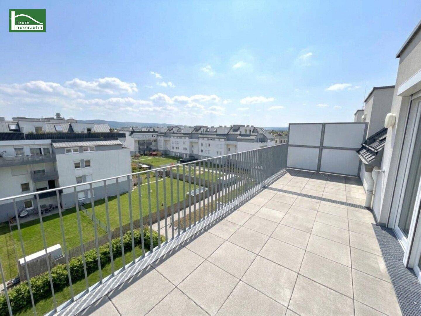Große Dachterrasse mit Fliesenboden und Blick auf die umliegenden Gebäude und Grünflächen.