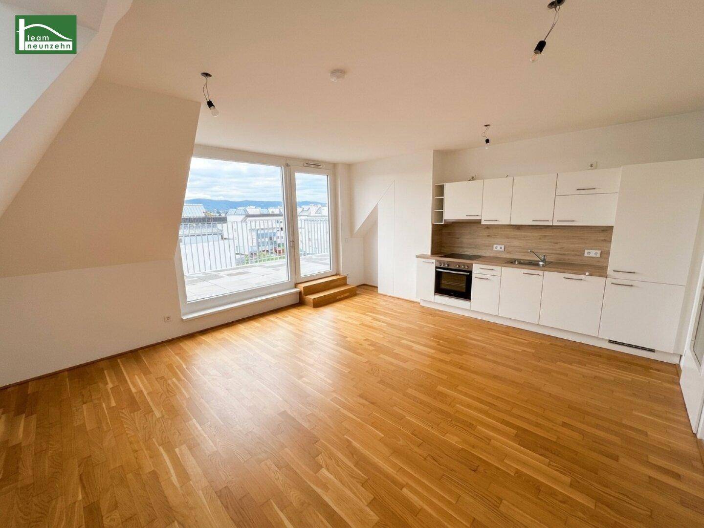 Geräumiges, leeres Wohn-Esszimmer mit offener Küchennische, Parkettboden und Terrassenzugang.