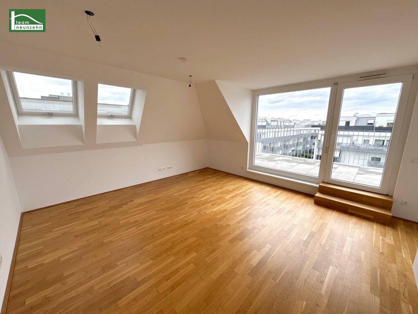 Heller, leerer Raum im Dachgeschoss mit Parkettboden, Dachfenstern und Terrassenzugang.