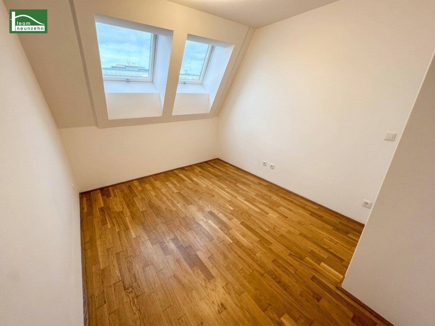 Leeres Arbeitszimmer im Dachgeschoss mit Parkettboden und zwei Dachfenstern.
