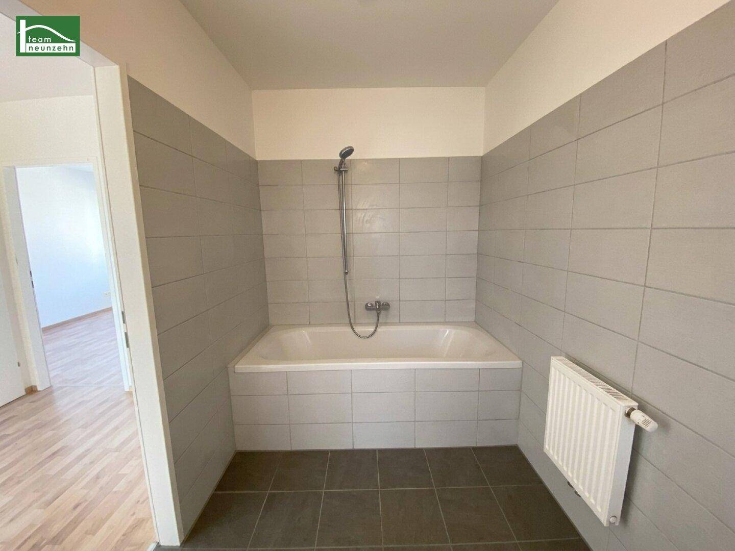 Badezimmer mit eingebauter Badewanne und grauen Wand- und Bodenfliesen, funktional und sauber.