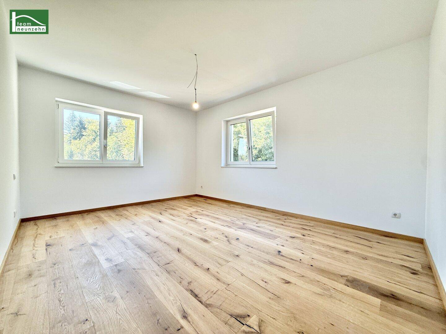 Heller, unmöblierter Raum mit zwei Fenstern und ansprechendem Holzboden.