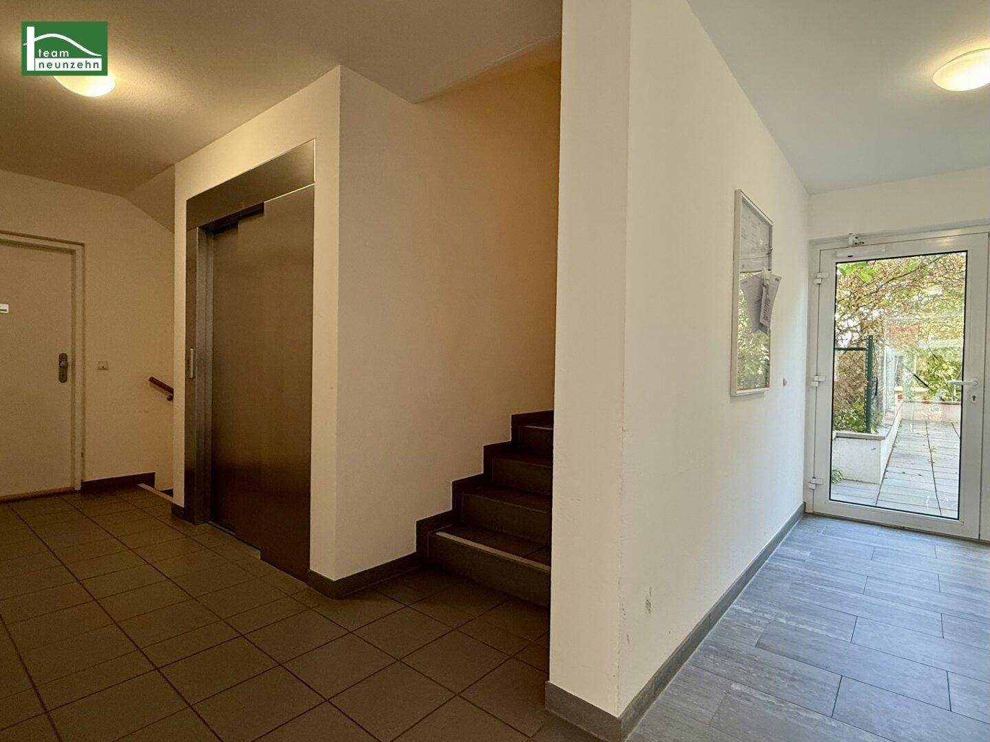 Eingangsbereich mit Aufzug, Treppe und Zugang zum Außenbereich durch eine Glastür, hell und einladend.