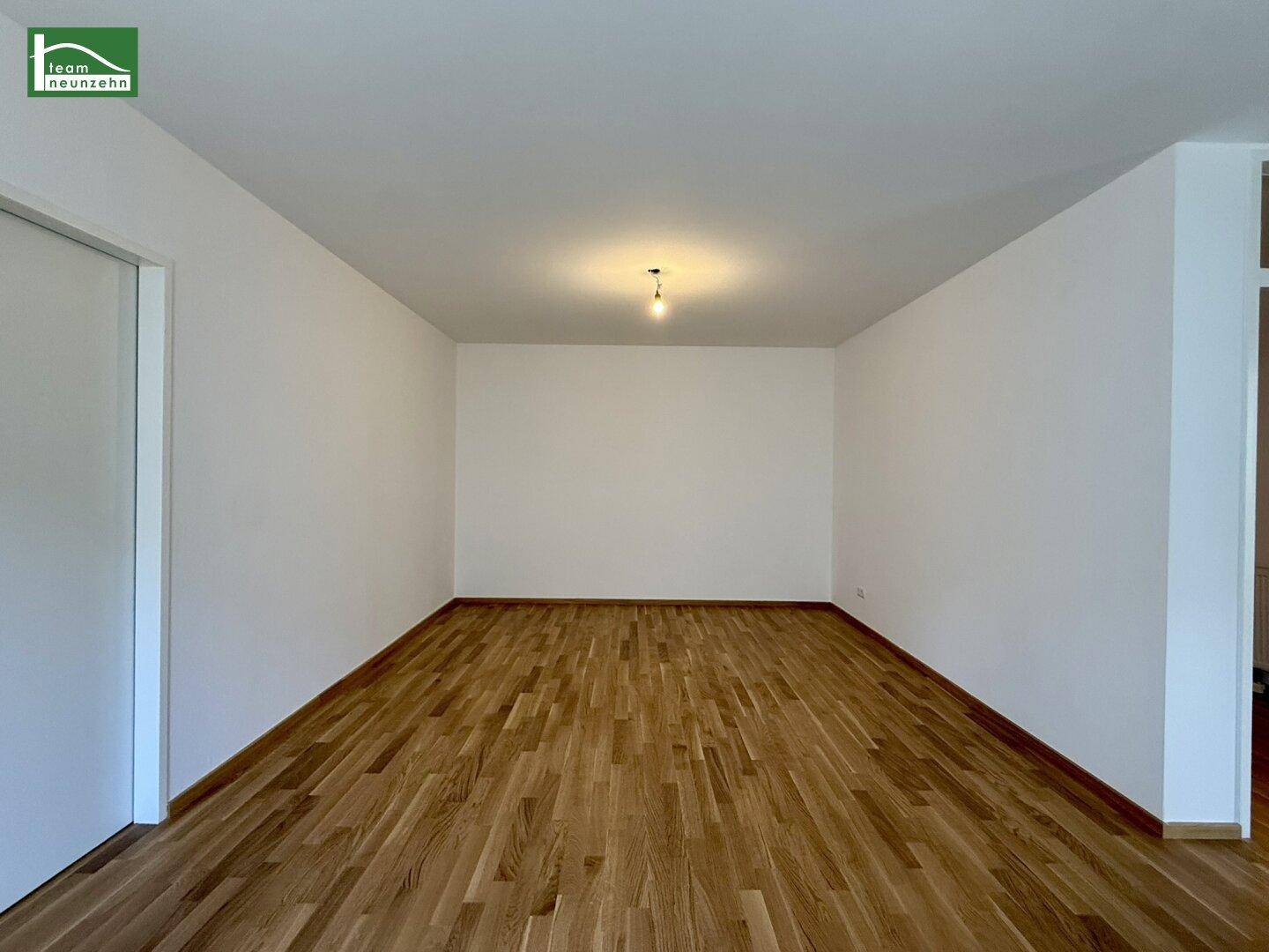 Leeres Zimmer mit hellem Holzparkettboden und einer einfachen Deckenleuchte, bereit zur individuellen Gestaltung.