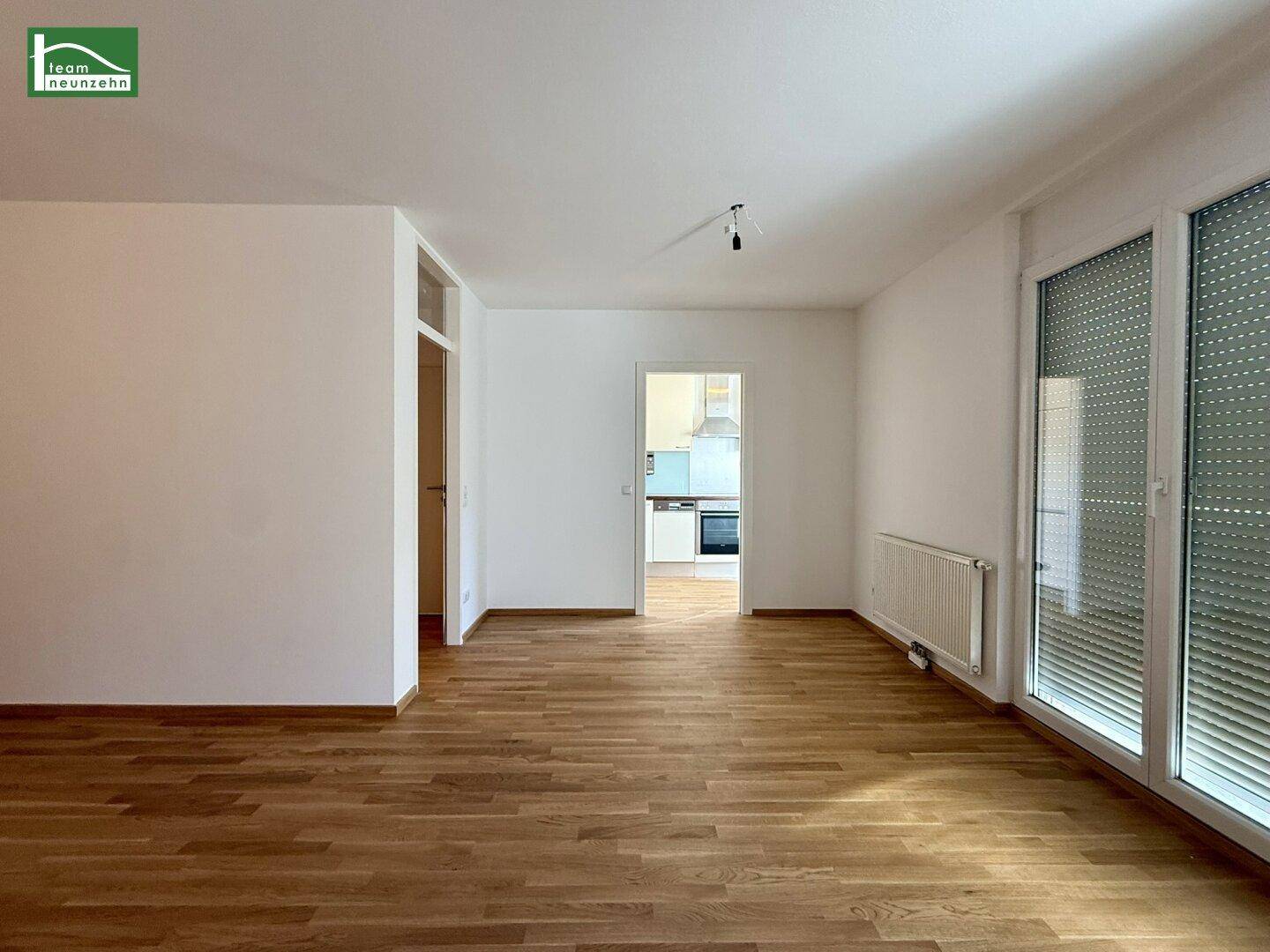 Heller, leerer Wohnbereich mit Holzparkettboden und Zugang zu einem Balkon.